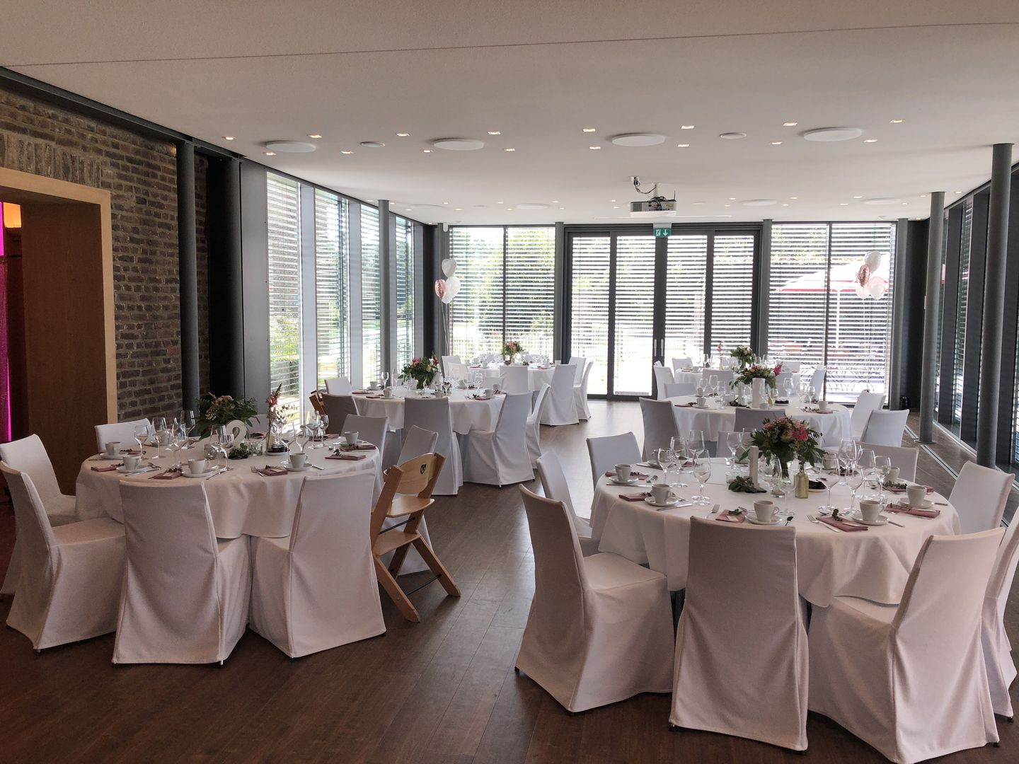 Heller Festsaal mit rund eingedeckten Tischen, weißen Hussen und Blumenschmuck