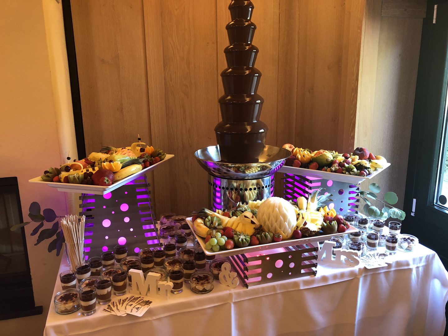 Schokoladenbrunnen zwischen beleuchteten Obstetageren und kleinen Dessertgläsern